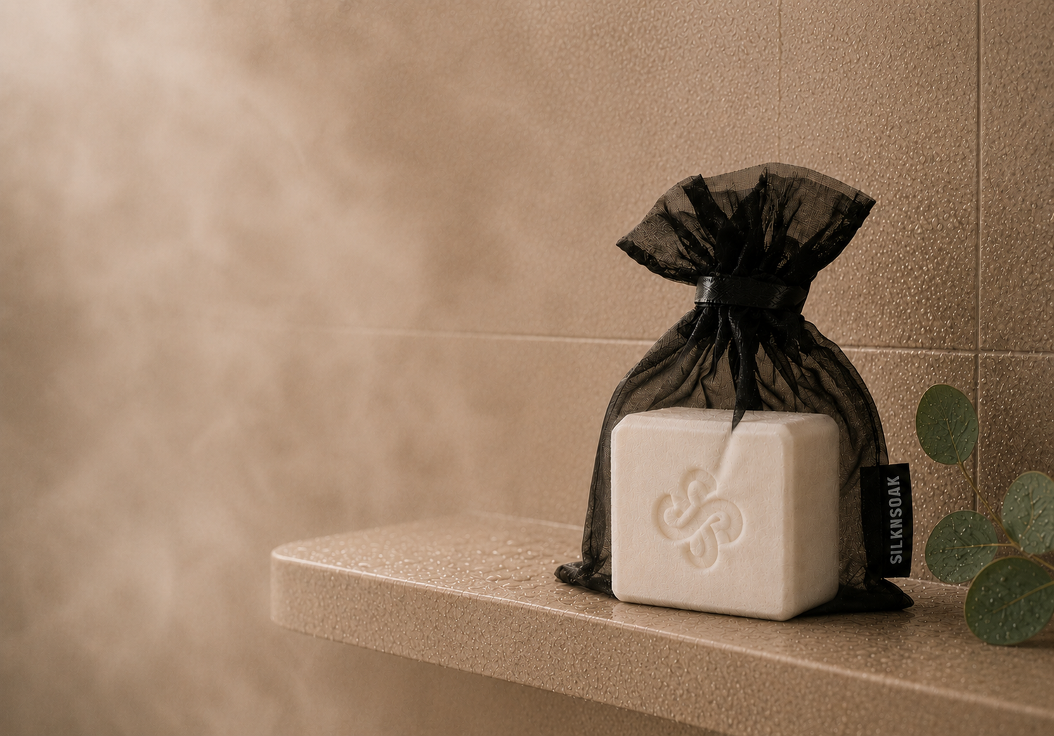 Silknsoak shower steamer cube in a black organza bag inside a warm steam-filled shower setting.